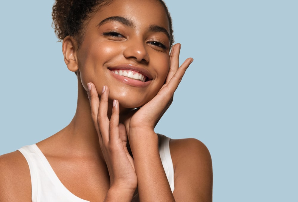 Smiling woman with clear skin, hands gently touching her face.