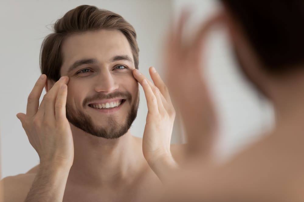 Man smiling while touching his face in a mirror.