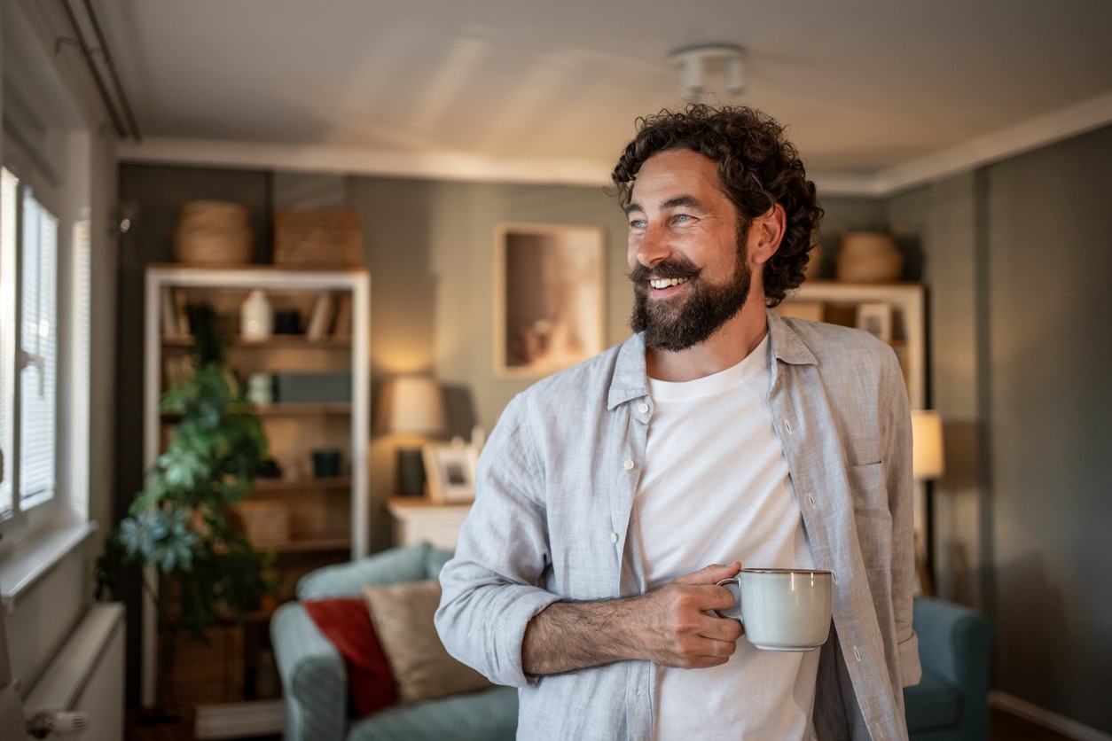 Man smiling while holding a mug in a cozy living room.